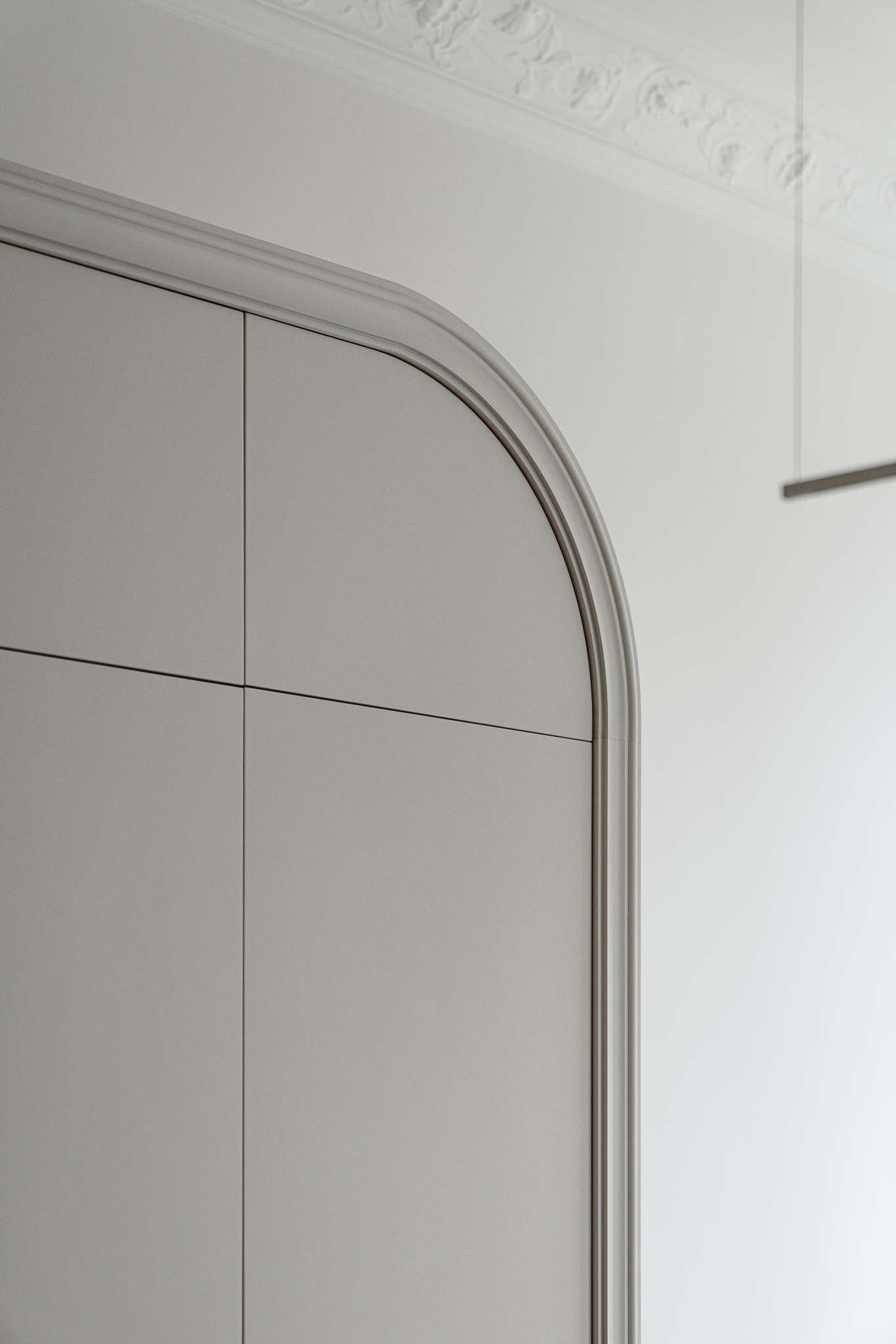 This kitchen pairs sculptural softness with practical sophistication. A central island in marble-look stone anchors the space, its clean lines echoed in the curved cabinetry and arched built-ins. Walnut lower cabinets add warmth and grain, while open shelving displays a curated mix of ceramics and glassware. 